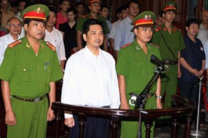 Cu Huy Ha Vu (C) stands between policemen in the dock during his trial at a court in Hanoi, August 21, 2011.