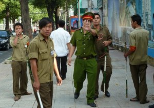 A policeman, flanked of local milicia members, tries to stop a foreign journalist from taking pictures as they guard outside the Ho Chi Minh City People's Court on August 10, 2011 where Pham Minh Hoang, a French-Vietnamese lecturer and blogger is standing trial, facing up to 15 years' jail on a subversion charges in the country's latest high-profile rights case.  AFP PHOTO / IAN TIMBERLAKE