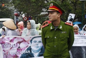 A policeman stands in front of supporters of lawyer Le Quoc Quan, as they hold a banner of him outside a court in Hanoi, 18 February 2014