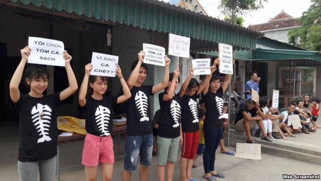 FILE - Protesters hold signs about the mass fish deaths in Nghe An Province, central Vietnam. Protests Sunday led to dozens of people being detained by police in Hanoi and Ho Chi Minh City.