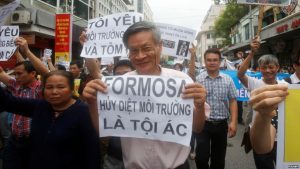 Political dissident Nguyen Quang A (C) holds a sign which reads "Formasa - damaged the environment and is a criminal" during a protest in Hanoi, Vietnam, May 1, 2016.